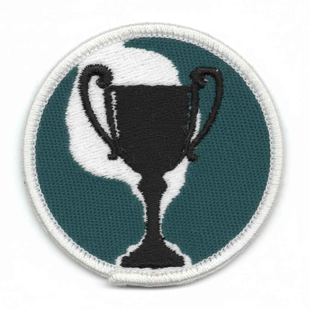 Parche bordado con diseño de trofeo negro sobre fondo verde y blanco, bordeado en hilo blanco.