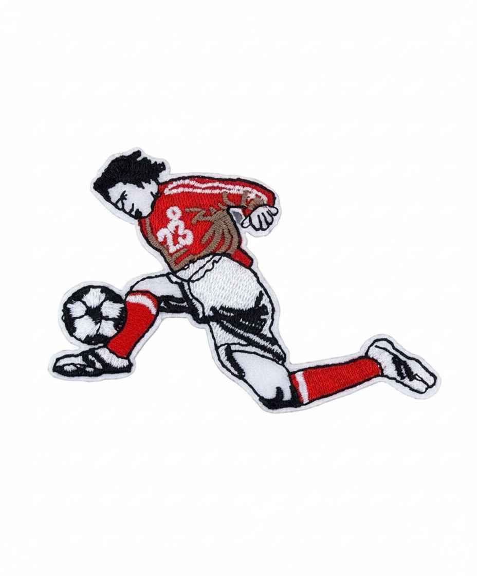 Parche bordado de futbolista con camiseta roja y pantalones blancos pateando un balón blanco y negro.